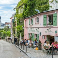 people are sitting at tables in front of pink buildings with green shutters on the windows