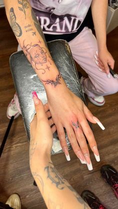 two women with tattoos on their arms and hands, one holding the other's hand