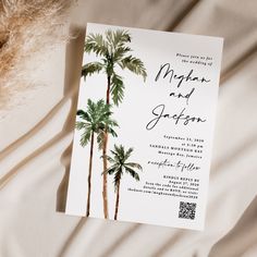 a wedding card with palm trees on it sitting on top of a white bed sheet