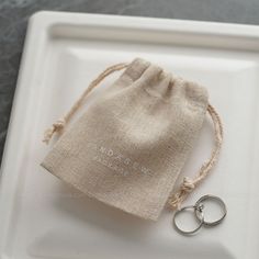 two wedding rings sitting on top of a white tray next to a drawstring bag