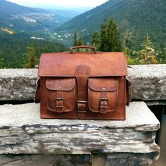 a brown leather bag sitting on top of a stone wall next to a mountain range