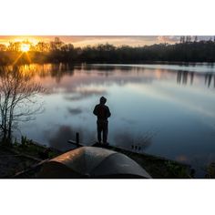 a man standing on the edge of a lake at sunset