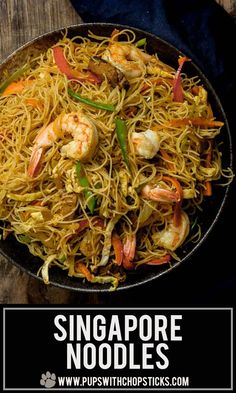 a pan filled with noodles and shrimp on top of a wooden table