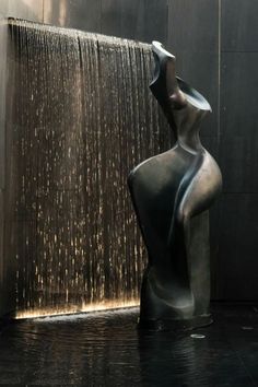 a large metal statue sitting next to a wall with water pouring from it's sides