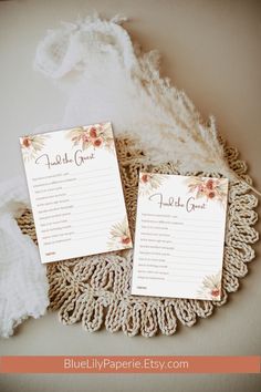 two wedding program cards sitting on top of a doily with feathers in the background