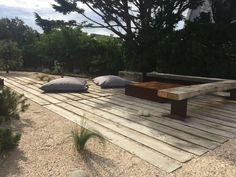 some pillows are sitting on a wooden platform in the middle of a garden area with trees and bushes