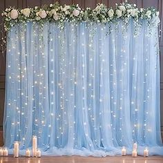 a blue backdrop with white flowers and candles on the floor in front of it for a wedding ceremony