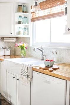 a kitchen with white cabinets and wooden counter tops, along with a window over the sink