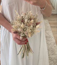 a woman in white dress holding a bouquet of flowers on carpeted floor next to wall