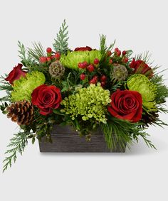 a wooden box filled with flowers and greenery on top of a white table next to a pine cone