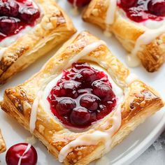 cranberry crescent pastries on a plate with cherries around the edges and drizzled with icing