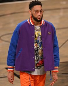 a man in an orange and blue jacket is walking down the court with his hand on his hip