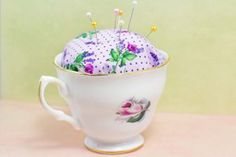 a cup with some pins in it and flowers on the inside, sitting on a table