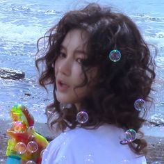 a woman standing on top of a beach next to the ocean with bubbles in her hair