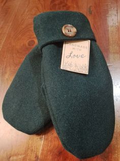 a pair of green mittens with a tag on it sitting on a wooden floor