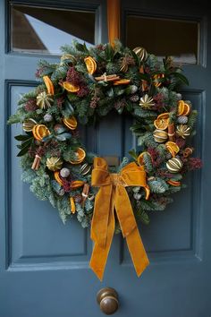 a christmas wreath hanging on a blue door with yellow ribbon and bells attached to it