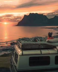 an image of a person laying on top of a van with the sun setting in the background