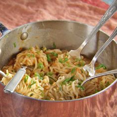 a pot full of noodles with two spoons in it on a tableclothed surface