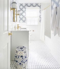 a white bathroom with blue and white tiles on the floor, shower curtain, and stool