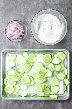 sliced cucumbers and onions on a tray with dip in the bowl next to them