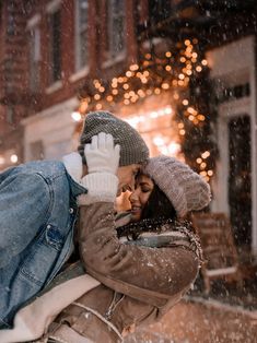 a man and woman kissing in front of a building with snow falling on the ground