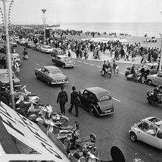 black and white photograph of people walking on the street in front of cars, motorcycles and motorcyclists