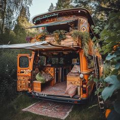 an orange bus parked in the middle of a forest filled with lots of trees and plants