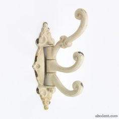 an ornately carved white wall hook on a white background with the letter s in it's center