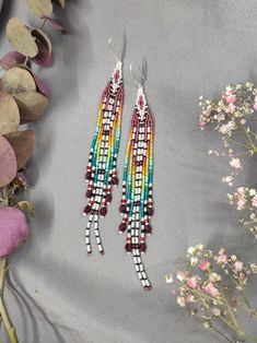 the multicolored beaded earrings are on display next to some pink and white flowers