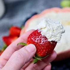 a hand holding a strawberry with whipped cream on it