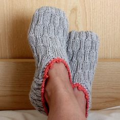 a person's feet wearing gray knitted slippers on top of a bed