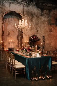 a table set up with candles and flowers in front of an old brick wall for a formal function