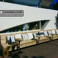 an outdoor seating area with wooden benches and white walls in front of a storefront