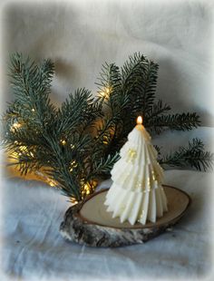 a small white christmas tree sitting on top of a piece of wood next to a lit candle