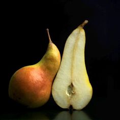 two pears with one cut in half and the other whole on a black background