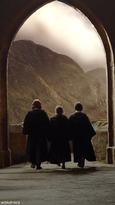 three people standing in front of an arch with mountains in the background and foggy sky