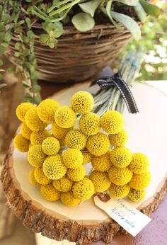 yellow flowers sitting on top of a tree stump next to a basket filled with greenery