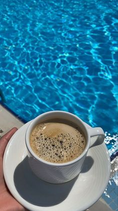 a cup of coffee sitting on top of a saucer next to a swimming pool