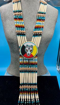 Bone hairpipes and crystal beads are often seen as part of traditional Native American dancers.  This modified breastplate  has been created to proudly proclaim that this is a good day to be Indigenous . It is designed to be worn not only in the dance circle, but in mainstream life, showing your Native pride and fashion sense.   The necklace is 10 vertical strands of bone hairpipes, nickel beads and 8mm sparking, faceted, fire-polished glass crystal beads in the colors of Snow White, emerald green, pale green, lilac and amethyst purple.  The centerpiece is a beaded rosette of a Wolf with golden eyes and a genuine turquoise cabochon on her forehead. She is surrounded by the colors of the Four Directions and lined with turquoise beads of the sky. The breastplate is done with sparkling facete Bone Bead Necklace, Breast Plate, Native American Clothing, Native Pride, Wolf Face, Earrings Patterns, Bone Necklace, Golden Eyes, Wolf Spirit