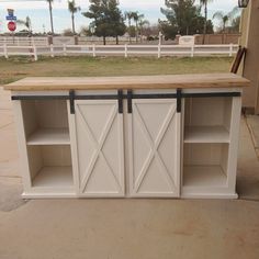 a white kitchen island with sliding doors on the top and bottom, in front of a fence