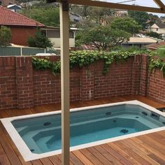 an outdoor hot tub with wooden decking next to brick wall and fenced in area