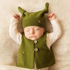 a baby is sleeping wearing a green hat and vest with buttons on it's ears