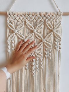 a woman's hand is touching the wall hanging made with macrame yarn