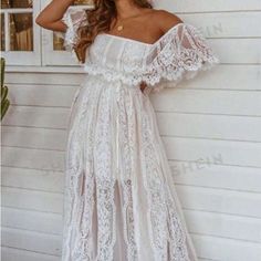 a woman standing in front of a house wearing a white dress with sheer lace on it