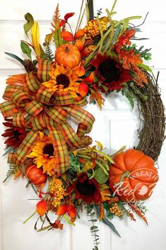 a wreath with pumpkins, sunflowers and other autumn decorations hanging on a door