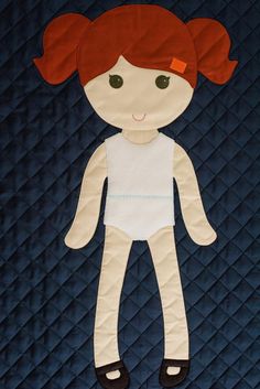 a quilted doll with red hair and black shoes on it's feet, sitting on a blue quilt