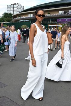 two women in white outfits are walking down the street while people watch from behind them