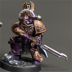 a purple and gold painted warhammer with two swords in his hand, on a black base