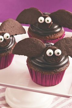 three cupcakes with chocolate frosting and decorated like bats on top are sitting on a white plate