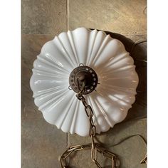 a white flower shaped light hanging on a wall next to a metal hook and chain